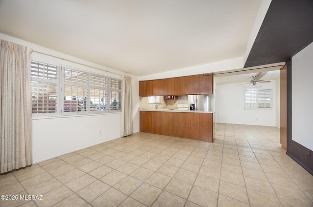 kitchen featuring sink, light tile patterned floors, stainless steel fridge with ice dispenser, decorative backsplash, and kitchen peninsula