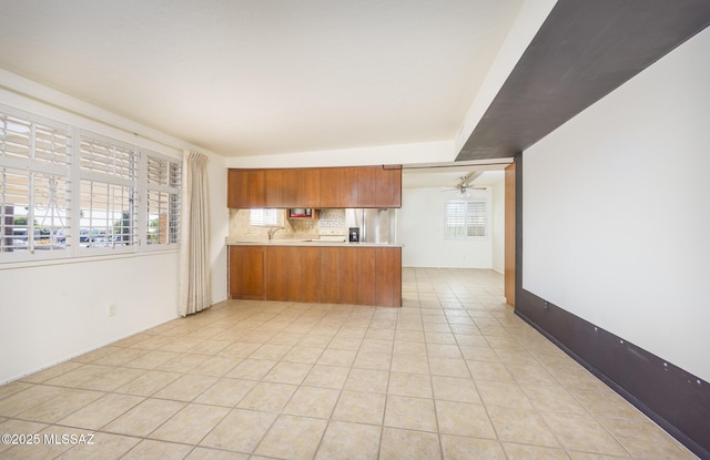 kitchen featuring sink, light tile patterned floors, kitchen peninsula, ceiling fan, and decorative backsplash