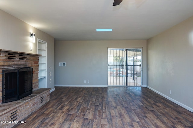 unfurnished living room featuring built in shelves, a fireplace, dark hardwood / wood-style floors, and ceiling fan