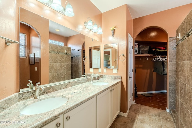bathroom featuring a walk in closet, a sink, double vanity, and tiled shower