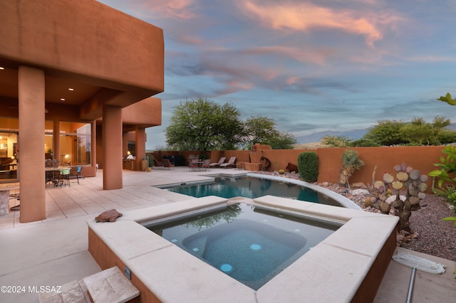 pool at dusk with an in ground hot tub and a patio area