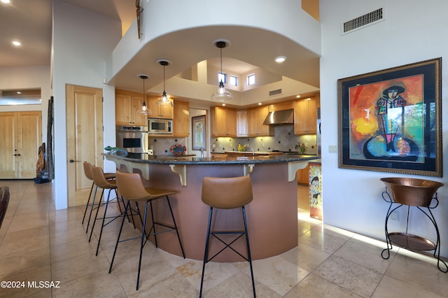 kitchen featuring stainless steel appliances, a breakfast bar, a towering ceiling, visible vents, and wall chimney exhaust hood