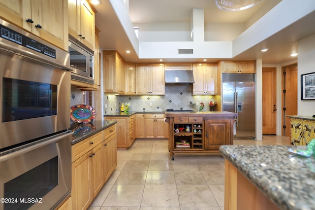 kitchen with built in appliances, dark stone countertops, a tray ceiling, decorative backsplash, and exhaust hood