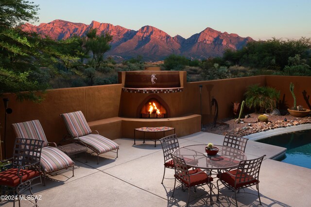 view of patio featuring a warm lit fireplace, a fenced in pool, a mountain view, and fence