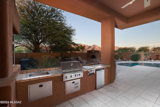 patio terrace at dusk featuring a fenced in pool, sink, a grill, a mountain view, and area for grilling