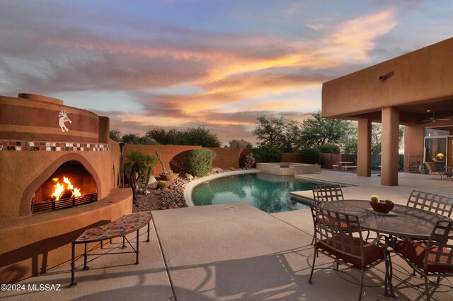 pool at dusk featuring an outdoor fireplace, an in ground hot tub, and a patio area