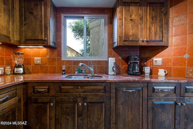 kitchen with light stone countertops, dark brown cabinetry, tasteful backsplash, and sink