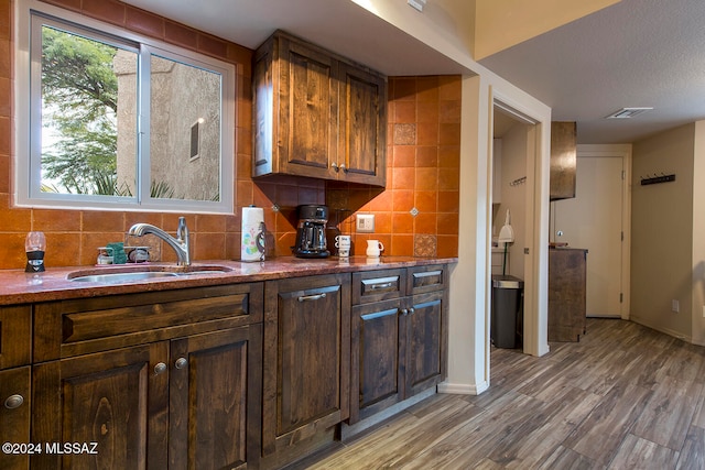 bar featuring decorative backsplash, light wood-type flooring, a textured ceiling, dark brown cabinetry, and sink