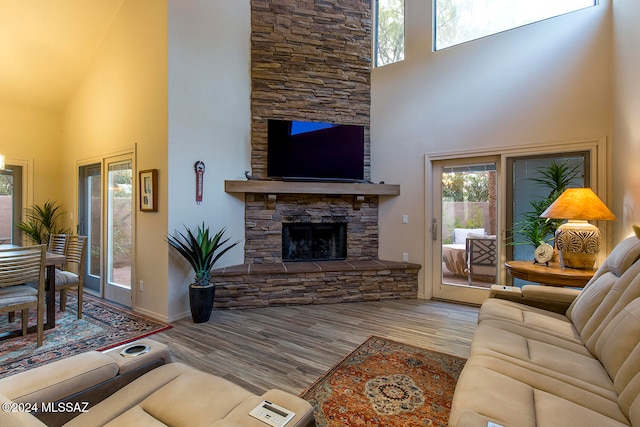 living room with a stone fireplace, a towering ceiling, and light wood-type flooring