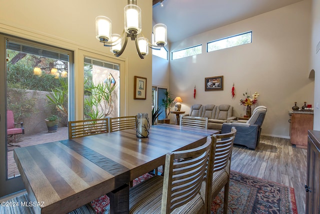 dining space featuring a wealth of natural light, hardwood / wood-style floors, a towering ceiling, and an inviting chandelier