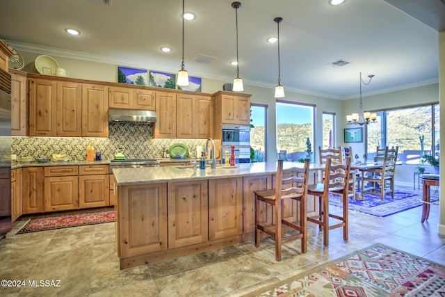 kitchen featuring tasteful backsplash, sink, pendant lighting, an inviting chandelier, and an island with sink