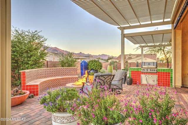 patio terrace at dusk with an outdoor kitchen, area for grilling, a mountain view, and a pergola