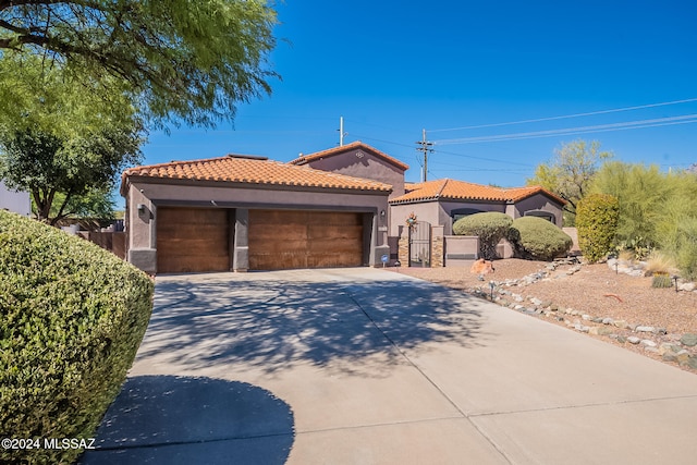 mediterranean / spanish-style home with an attached garage, a tiled roof, driveway, a gate, and stucco siding