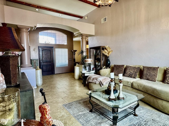 living area featuring arched walkways, stone tile floors, visible vents, a towering ceiling, and ornate columns