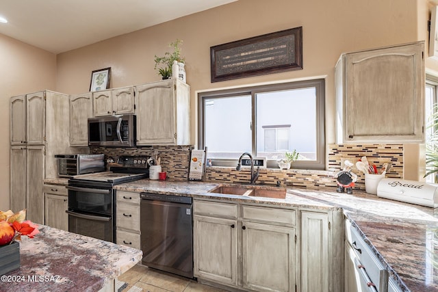 kitchen with a toaster, decorative backsplash, light stone countertops, black appliances, and a sink