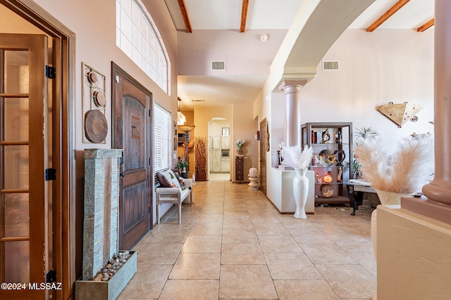 foyer with beamed ceiling, light tile patterned floors, and decorative columns