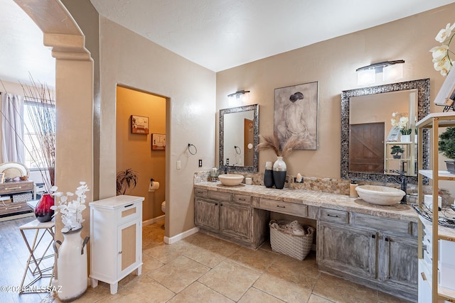 bathroom featuring double vanity, a sink, toilet, and baseboards