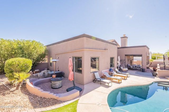 rear view of property with a chimney, a fire pit, a patio, and stucco siding