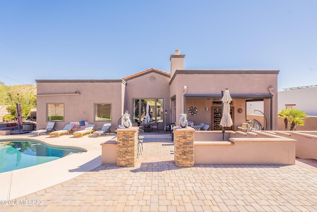 back of house with a patio area, a chimney, an outdoor pool, and stucco siding