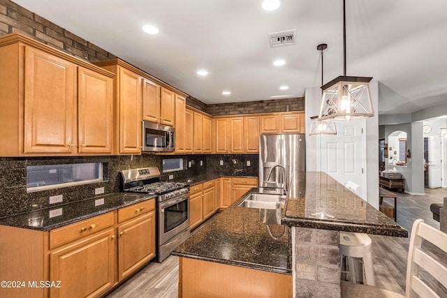 kitchen featuring appliances with stainless steel finishes, light wood-type flooring, a center island with sink, and hanging light fixtures