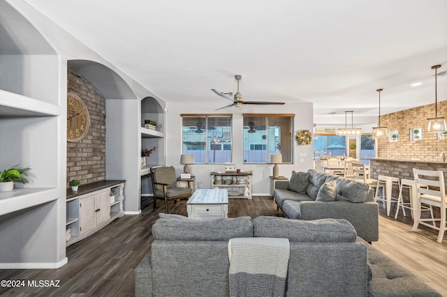 living room featuring ceiling fan, built in features, brick wall, and dark hardwood / wood-style floors