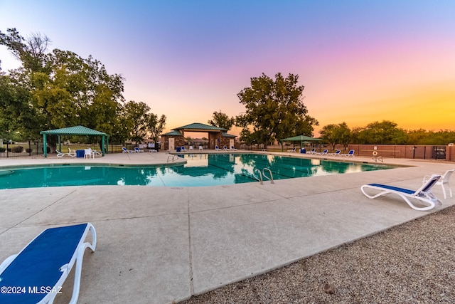 pool at dusk with a gazebo and a patio