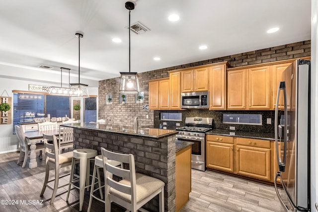 kitchen with a breakfast bar, stainless steel appliances, a center island, light hardwood / wood-style floors, and hanging light fixtures