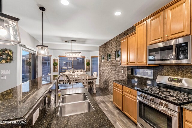 kitchen featuring sink, stainless steel appliances, dark stone countertops, pendant lighting, and hardwood / wood-style flooring