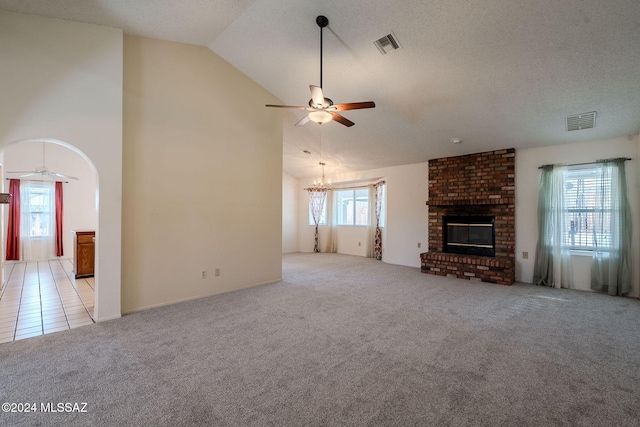 unfurnished living room with ceiling fan with notable chandelier, a textured ceiling, light tile patterned floors, high vaulted ceiling, and a fireplace