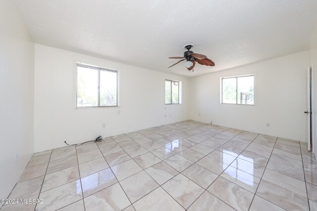 tiled empty room featuring ceiling fan and a textured ceiling