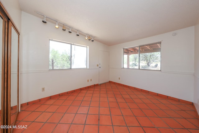 tiled empty room with a textured ceiling, plenty of natural light, and lofted ceiling