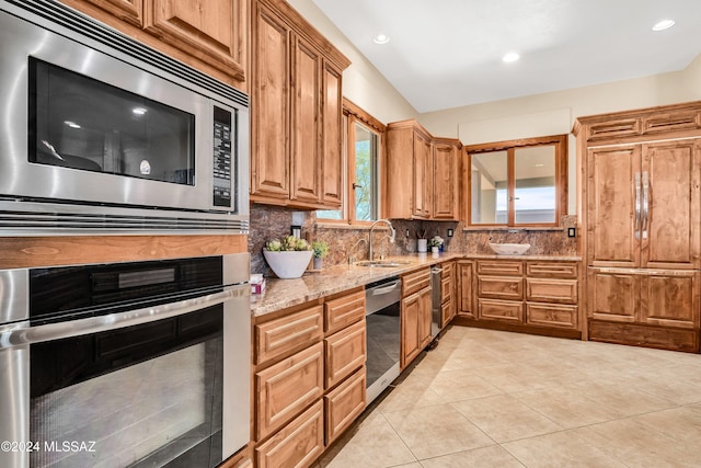 kitchen with light tile patterned floors, stainless steel appliances, a sink, backsplash, and light stone countertops