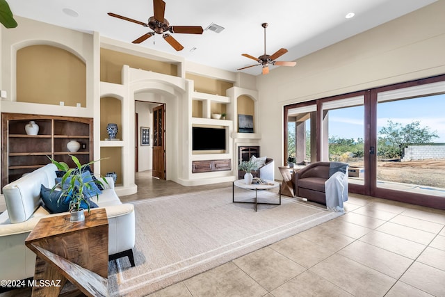 tiled living room featuring built in features, arched walkways, visible vents, a glass covered fireplace, and ceiling fan