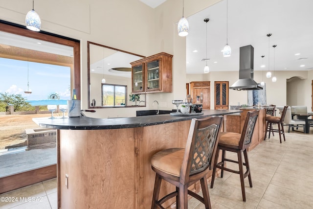 kitchen featuring island exhaust hood, glass insert cabinets, light tile patterned flooring, a sink, and a kitchen bar