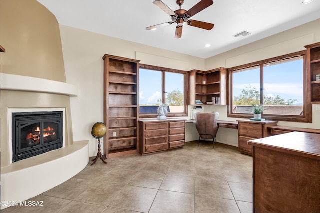 office area with a large fireplace, visible vents, built in study area, ceiling fan, and light tile patterned flooring