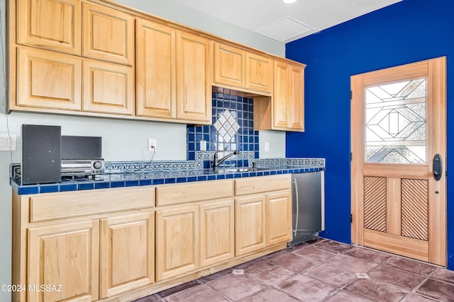 kitchen featuring visible vents, tile counters, decorative backsplash, stainless steel refrigerator, and light brown cabinets