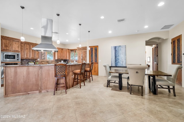 kitchen with arched walkways, island range hood, visible vents, brown cabinets, and stainless steel microwave