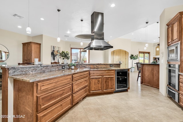 kitchen with wine cooler, visible vents, appliances with stainless steel finishes, brown cabinets, and island exhaust hood