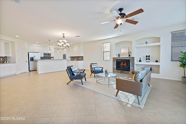 living room featuring built in shelves, a fireplace, ceiling fan with notable chandelier, and light tile patterned floors