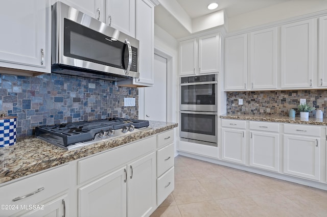 kitchen featuring light tile patterned flooring, stone countertops, white cabinetry, appliances with stainless steel finishes, and backsplash