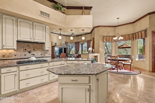 kitchen with stainless steel gas cooktop, hanging light fixtures, stone counters, kitchen peninsula, and ceiling fan with notable chandelier