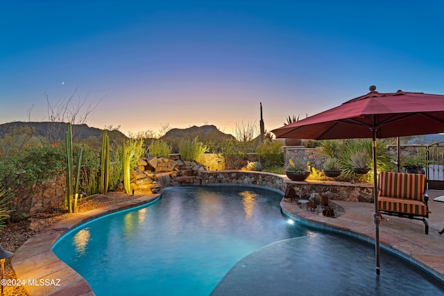 pool at dusk featuring a mountain view, pool water feature, and a patio area