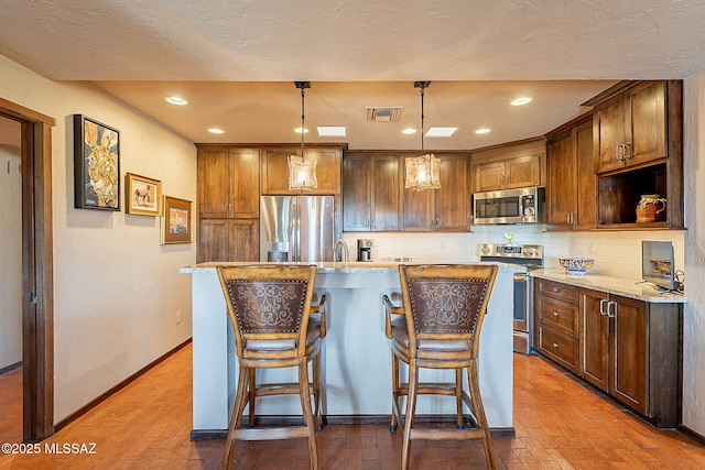 kitchen with backsplash, stainless steel appliances, hanging light fixtures, and an island with sink