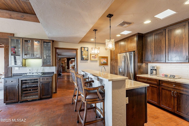 kitchen with a center island, hanging light fixtures, wine cooler, light stone countertops, and stainless steel fridge with ice dispenser