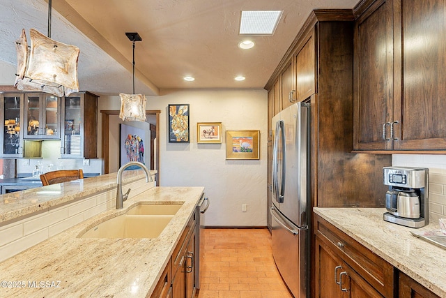 kitchen featuring backsplash, sink, hanging light fixtures, light stone countertops, and stainless steel appliances