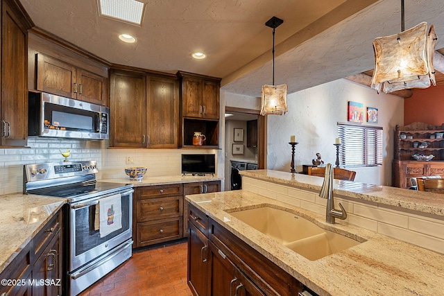 kitchen with sink, stainless steel appliances, light stone counters, decorative light fixtures, and decorative backsplash