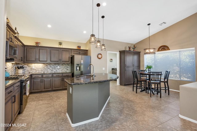 kitchen with decorative light fixtures, dark stone countertops, sink, a kitchen island with sink, and appliances with stainless steel finishes