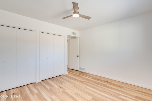 unfurnished bedroom with light wood-type flooring, ceiling fan, and two closets