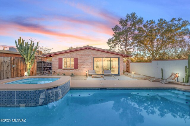 pool at dusk with an in ground hot tub and a patio