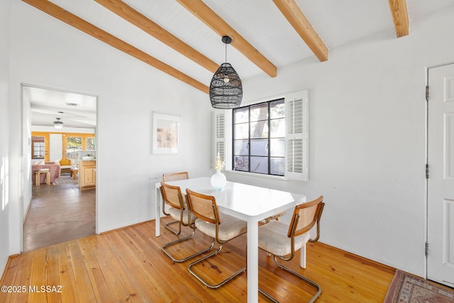 dining space featuring light wood finished floors and vaulted ceiling with beams